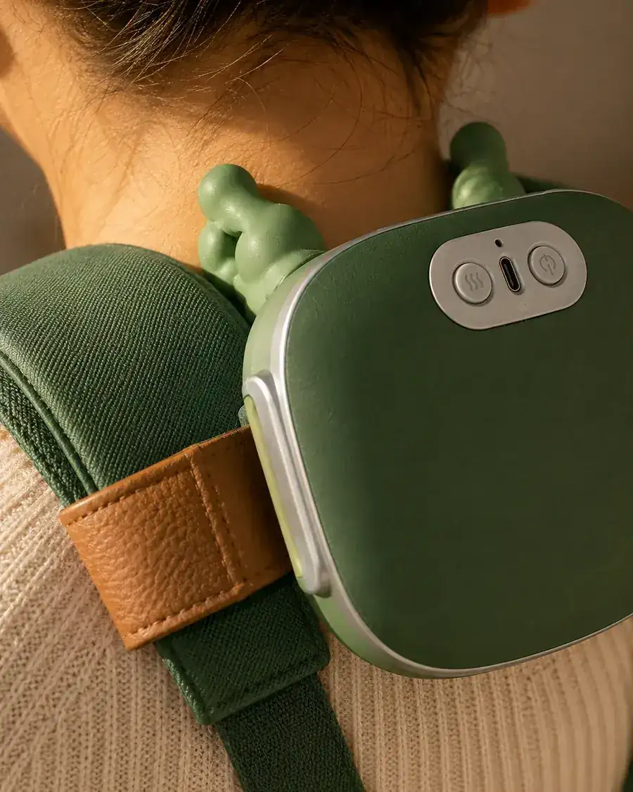 Macro view of the green shell resting against a shoulder, two silicone fingers curling over the trapezius
