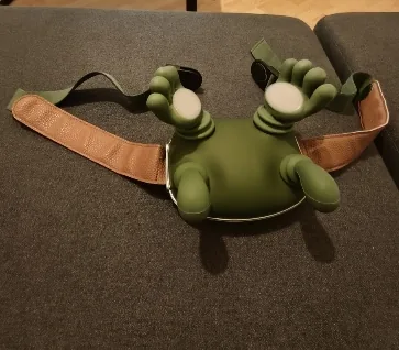 The Nodly massager resting on a grey sofa, its two heads and adjustable strap spread out